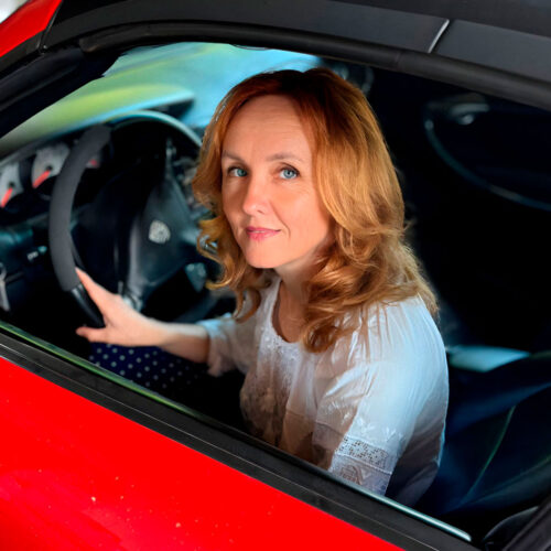 A woman wearing glasses and a green coat holds a white paper