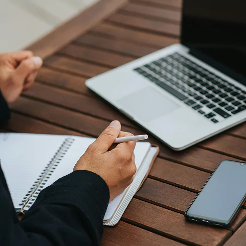 Businessman writing in a notebook while using a laptop
